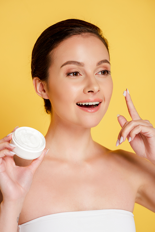 smiling beautiful woman with cosmetic cream on finger isolated on yellow