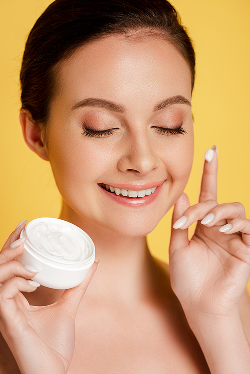 smiling naked beautiful woman with cosmetic cream on finger isolated on yellow