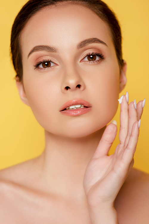 naked beautiful woman applying face cream isolated on yellow