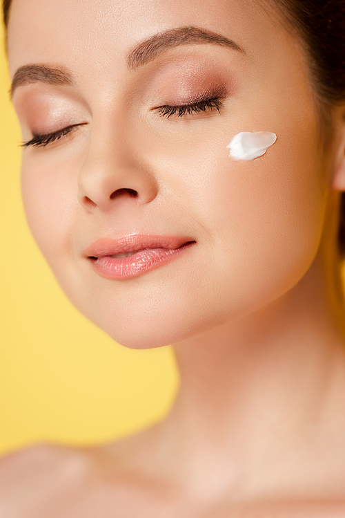 naked beautiful woman with cosmetic cream on face and closed eyes isolated on yellow