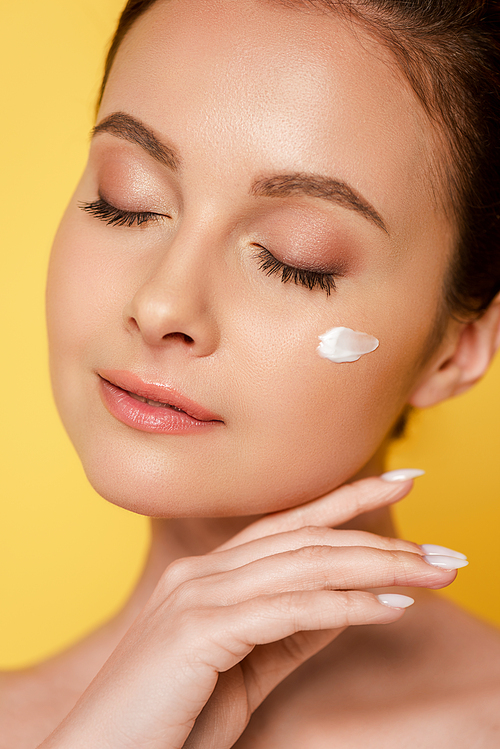 naked beautiful woman with cosmetic cream on face and closed eyes isolated on yellow