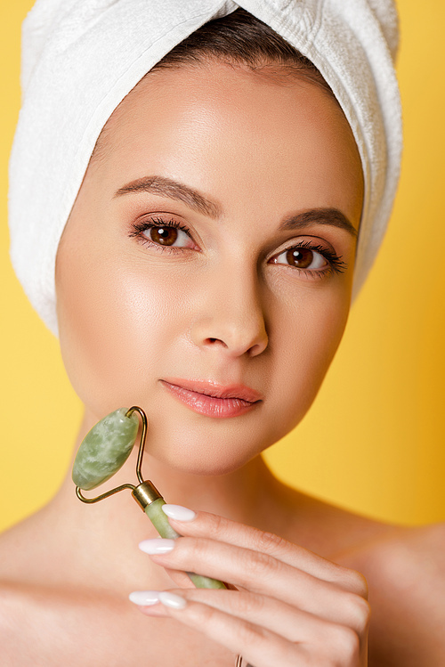 beautiful naked woman with towel on head using jade roller isolated on yellow