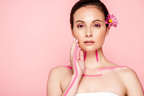 beautiful woman with pink lines on body and flower in hair touching face isolated on pink