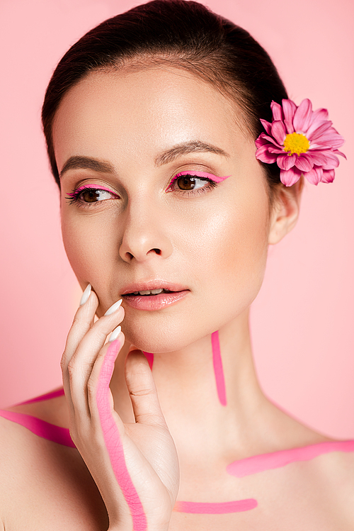 naked beautiful woman with pink lines on body and flowers in hair looking away isolated on pink