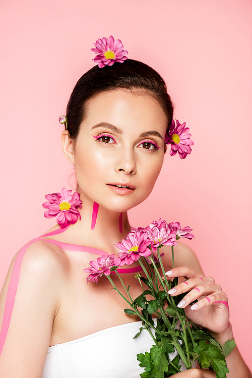 beautiful woman with pink lines on body and flowers in hair holding bouquet isolated on pink