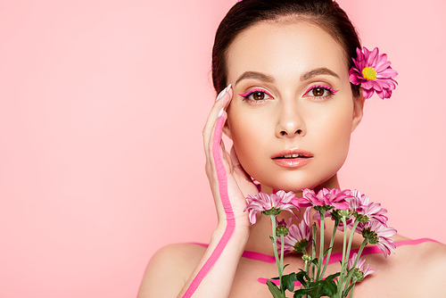 naked beautiful woman with pink lines on body and flower in hair holding bouquet and touching face isolated on pink