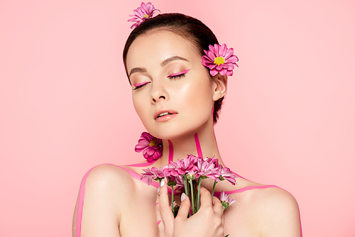 naked beautiful woman with closed eyes, pink lines on body and flowers in hair holding bouquet isolated on pink