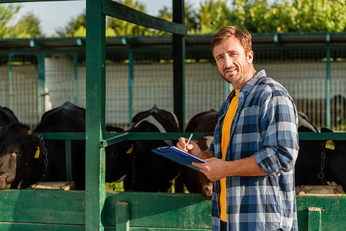 farmer in plaid shirt  while standing near cowshed and writing on clipboard