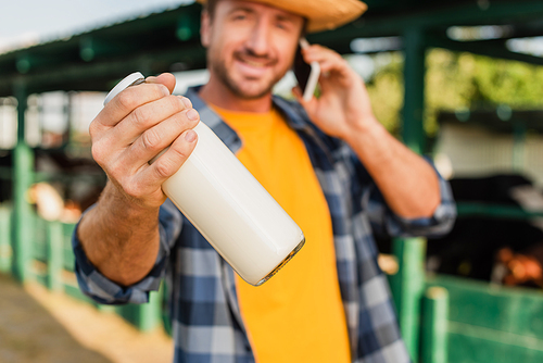 selective focus of farmer talking on smartphone and holding bottle of fresh milk while 