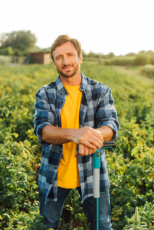 farmer in plaid shirt  while standing with shovel in field