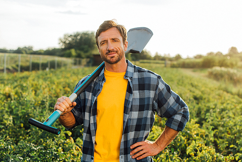 farmer in plaid shirt  while holding shovel in field