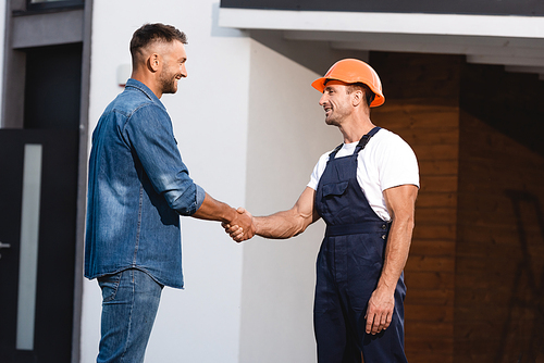 Man shaking hands with builder in uniform near building