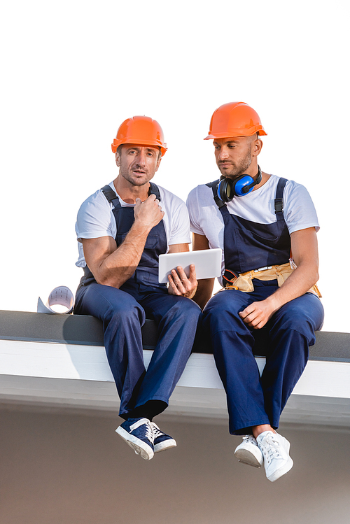 Builders using digital tablet while sitting on roof of building isolated on white