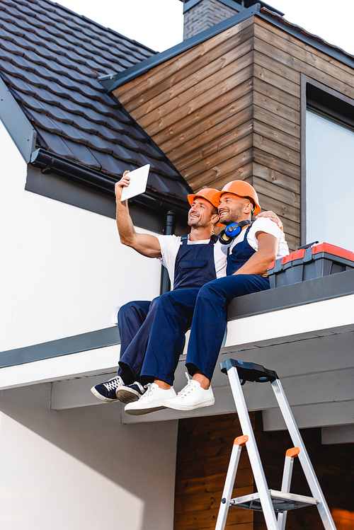 Builders taking selfie on digital tablet while sitting on roof of building