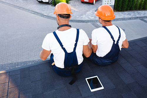 Back view of builders sitting near digital tablet on roof of building