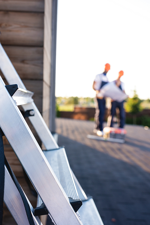 Selective focus of ladder and builders working on roof of house at background