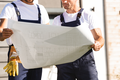 Cropped view of builders looking at blueprint outdoors