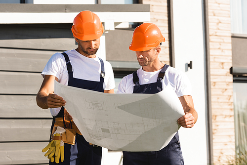 Builders holding blueprint while working near building