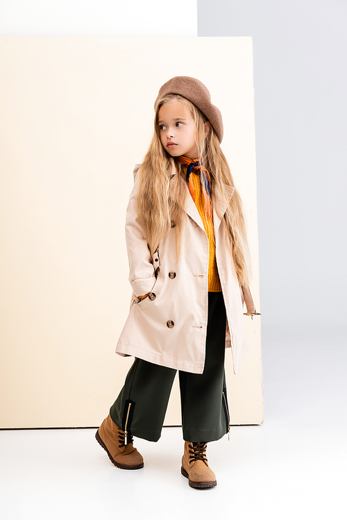fashionable blonde girl in autumn outfit looking away and walking on beige and white background
