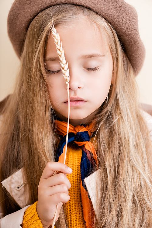 fashionable blonde girl with closed eyes in autumn outfit holding wheat spike