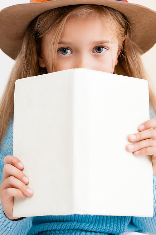 blonde girl in brown hat holding book in front of face