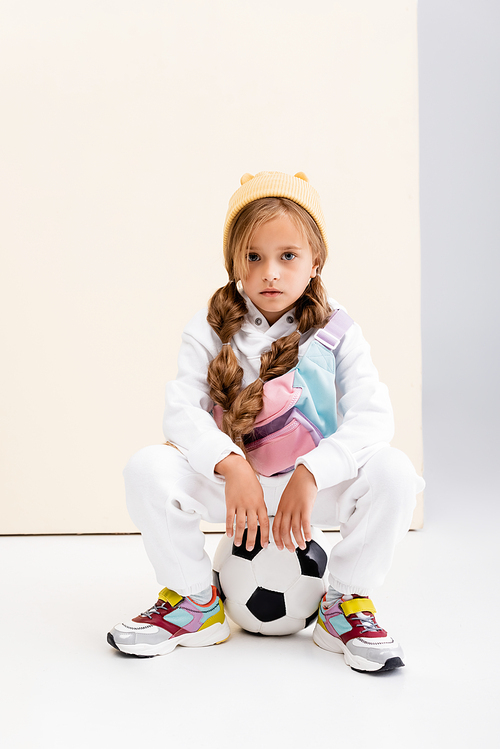 blonde girl in sportswear posing with soccer ball on beige and white background