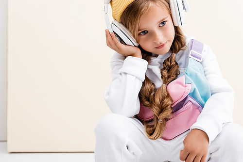 blonde girl in sportswear and headphones posing on beige and white background