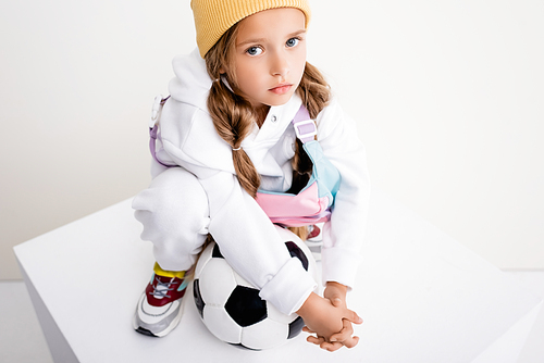 blonde girl in sportswear posing with soccer ball on cube on white