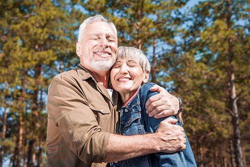 smiling senior couple of tourists embracing with closed eyes in sunny day