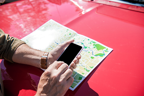 cropped view of man standing near red car with map and using smartphone with blank screen