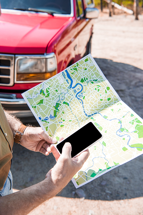 cropped view of man standing near red car with map and using smartphone with blank screen