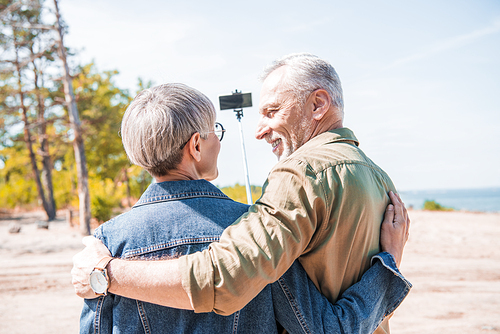 back view of senior couple embracing and taking selfie in sunny day
