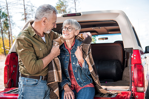 smiling senior couple sitting in car with blanket and looking at each other