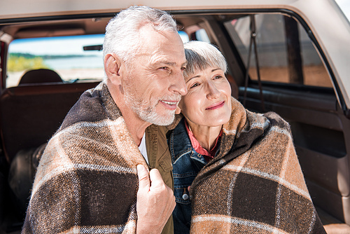 smiling senior couple sitting in car with blanket