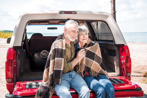 smiling senior couple sitting in car with blanket