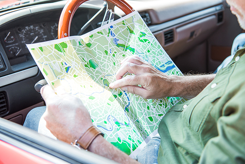 cropped view of senior man holding map in car