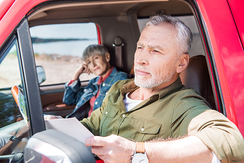 senior man holding map while sitting in car with wife