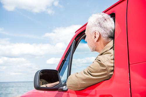 senior man looking at river from red car