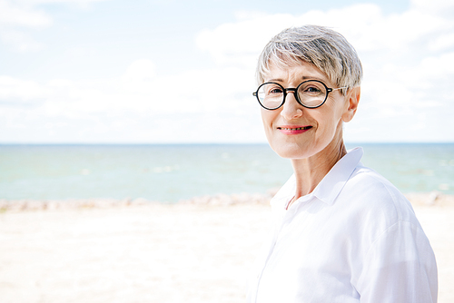 smiling senior woman in glasses and white shirt  at beach