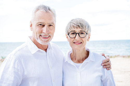 front view of smiling senior couple embracing and  at beach