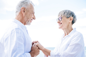 side view of happy senior couple holding hands and looking at each other in sunny day