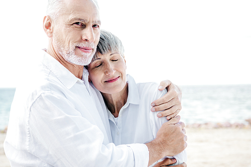 happy senior couple in white shirts embracing at beach