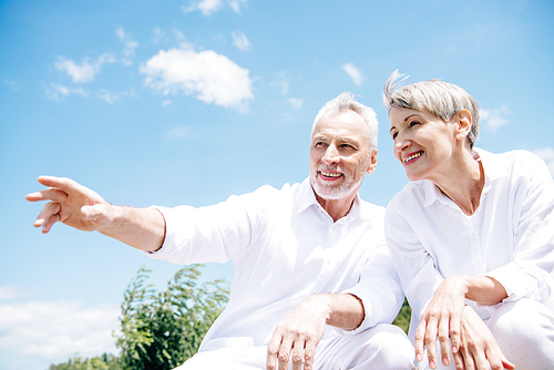 happy smiling senior couple in white shirts looking away under blue sky
