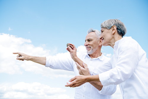 happy smiling senior couple holding stone and pointing with finger under blue sky