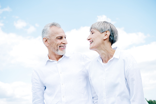 happy smiling senior couple in white shirts looking at each other under blue sky