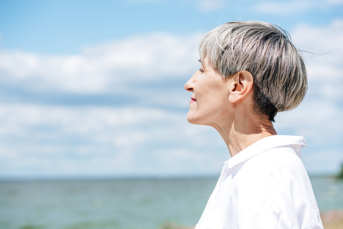 side view of senior woman in white shirt looking away near river in sunny day