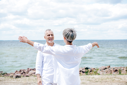 back view of senior woman embracing smiling husband at beach