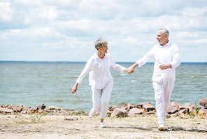 full length view of senior couple holding hands and looking at each other at beach
