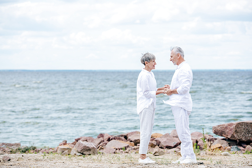 full length view of senior couple holding hands and looking at each other at beach