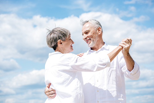 happy senior couple looking at each other while dancing under blue sky